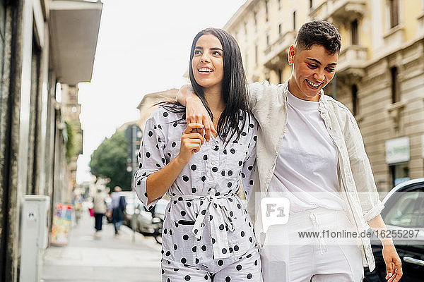Young lesbian couple walking arm in arm down a street.