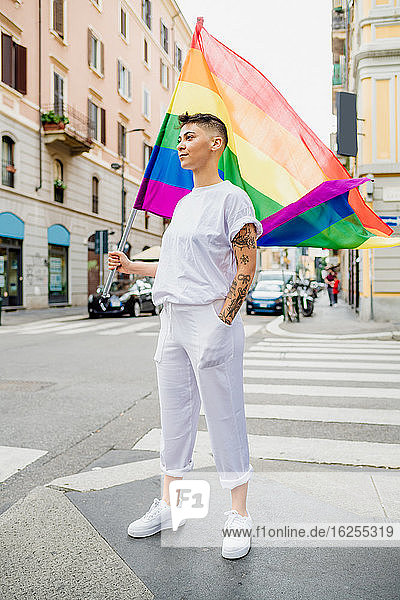 Young lesbian woman standing on a street  waving rainbow flag.