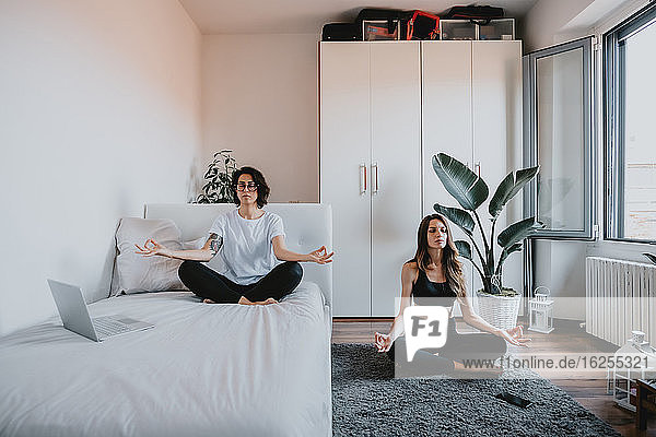 Zwei Frauen mit braunem Haar sitzen in einer Wohnung und meditieren.
