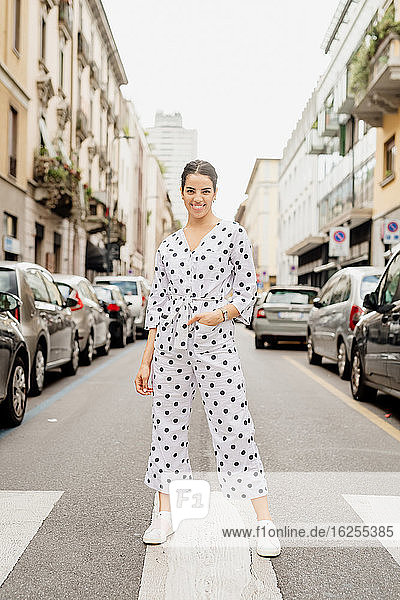 Portrait of smiling woman wearing white and black polka dot jumpsuit  standing on pedestrian crossing.