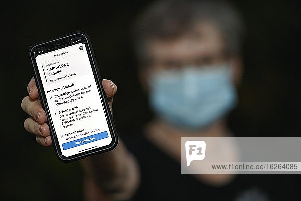 Negatives Testergebnis  Person mit Mundschutz zeigt Smartphone mit Corona Warn-APP  Corona-Krise  Baden-Württemberg  Deutschland  Europa