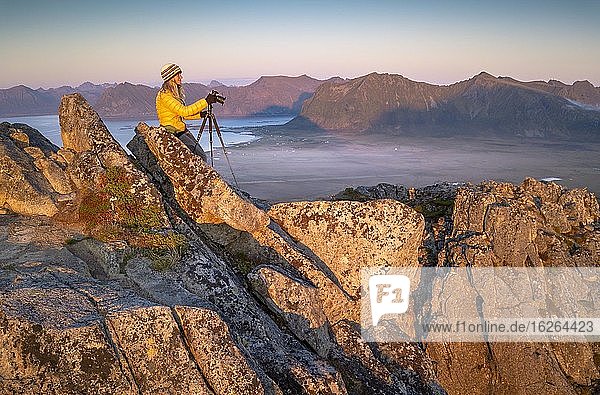 Fotografin mit Stativ am Gipfel des Hoven bei Sonnenuntergang  hinten dunstiges Tal und Meer  Vågan  Lofoten  Nordland  Norwegen  Europa