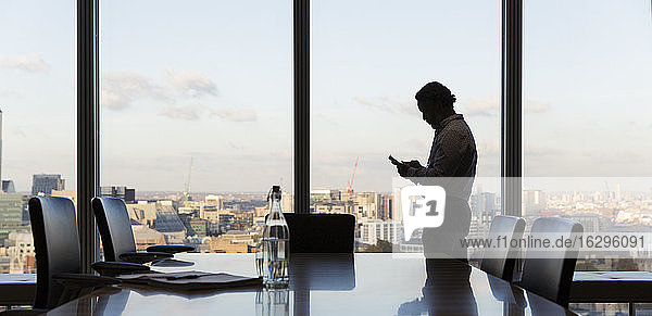 Geschäftsmann mit Smartphone am Fenster eines Hochhausbüros  London  Großbritannien