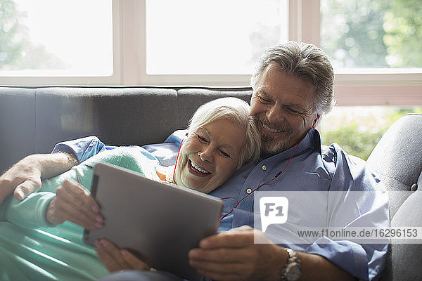 Happy senior couple sharing headphones and digital tablet on sofa