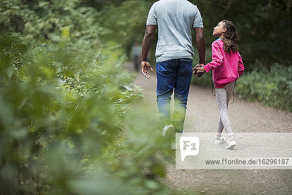Vater und Tochter halten sich beim Wandern auf Waldwegen an den Händen