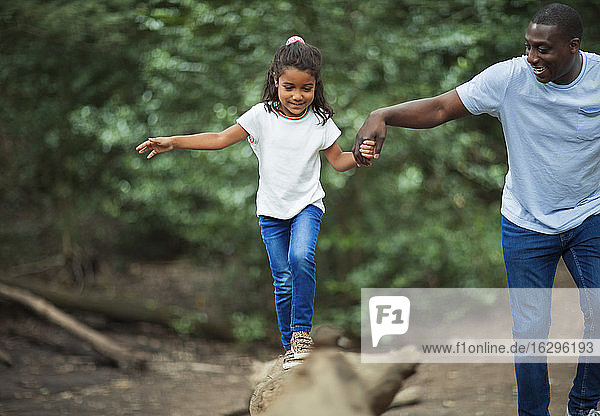 Vater hilft Tochter beim Balancieren auf gefallenem Baumstamm im Wald