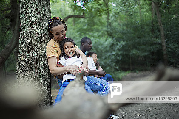 Glückliche Familie entspannt sich auf gefallenem Baumstamm bei Waldwanderung