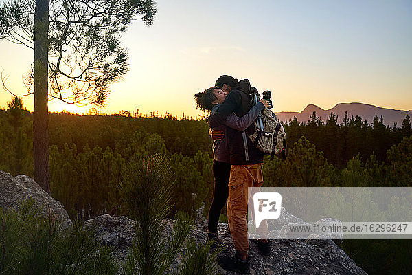 Liebenswertes junges Wandererpaar beim Wandern auf Fels in Wäldern bei Sonnenuntergang