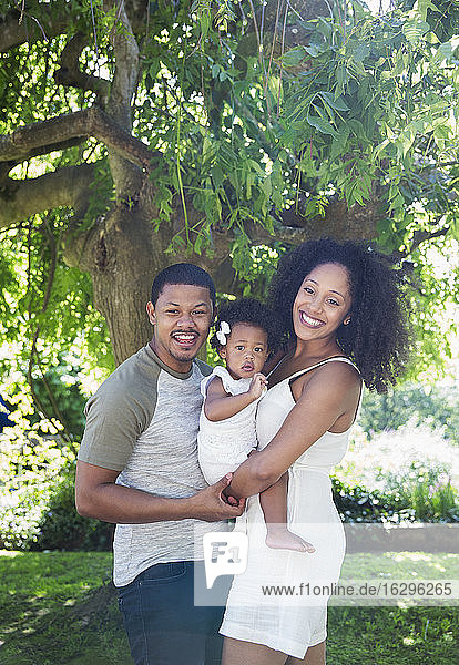 Porträt glückliche Eltern und Kleinkind-Tochter unter Baum im Sommergarten