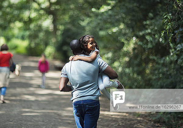 Playful father carrying happy daughter on trail in woods