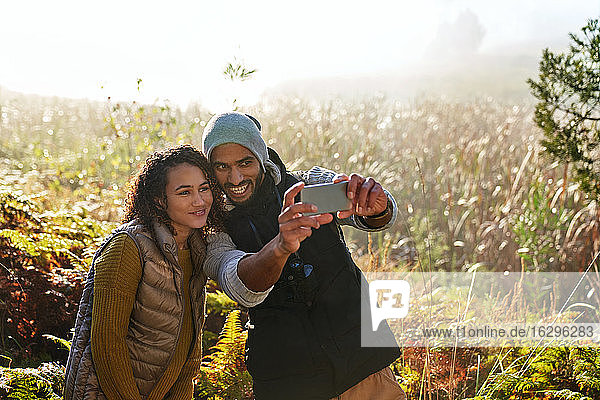 Glückliches junges Paar mit Fotohandy  das sich selbst im sonnigen hohen Gras fotografiert