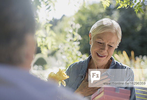 Glückliche ältere Frau erhält Geschenk von Ehemann auf sonniger Terrasse