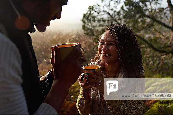 Glückliches junges Paar trinkt Kaffee in sonnigen Wäldern