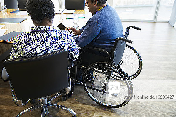 Geschäftsmann im Rollstuhl benutzt Smartphone im Konferenzraum