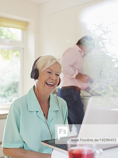 Glückliche ältere Frau mit Kopfhörern Video-Chat am Laptop in der Küche