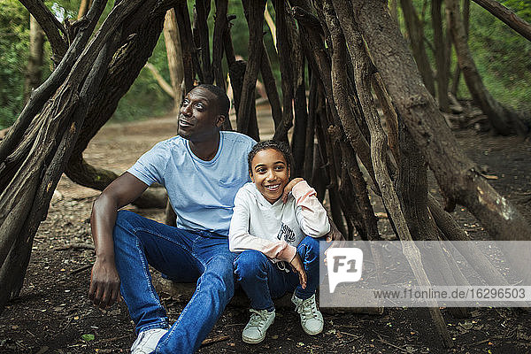 Glückliche Vater und Tochter entspannen sich in einem Baumäste-Tipi im Wald