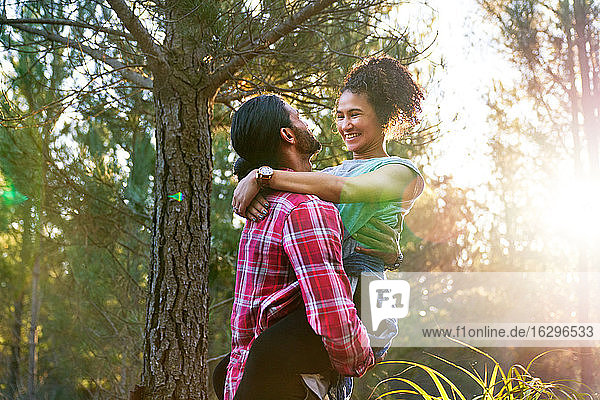 Affectionate young man holding happy girlfriend in sunny woods