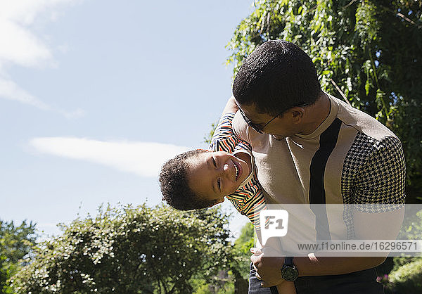 Playful father holding happy son in sunny summer backyard