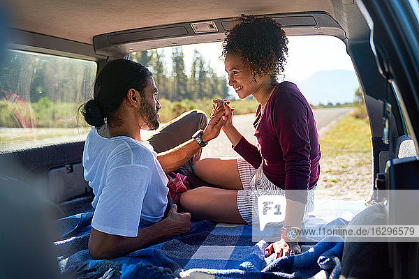 Glückliches  liebevolles  junges Paar hält Hände auf dem Rücksitz eines sonnigen Autos