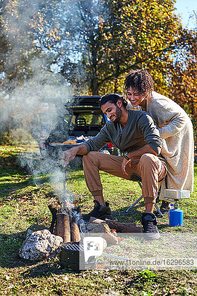 Glückliches junges Paar genießt Lagerfeuer im sonnigen Herbstfeld