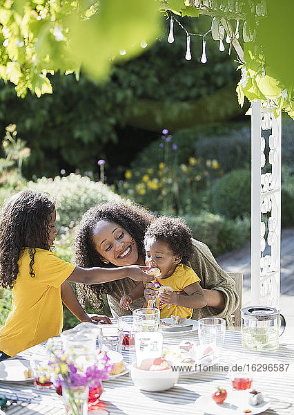 Glückliche Mutter und Töchter essen an einem sonnigen Sommer-Gartentisch