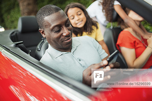 Mann benutzt Smartphone im Cabrio mit Familie