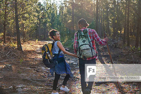 Happy young couple with backpacks hiking in sunny woods