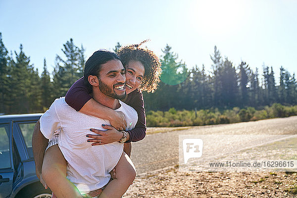 Happy affectionate couple piggybacking at sunny summer roadside