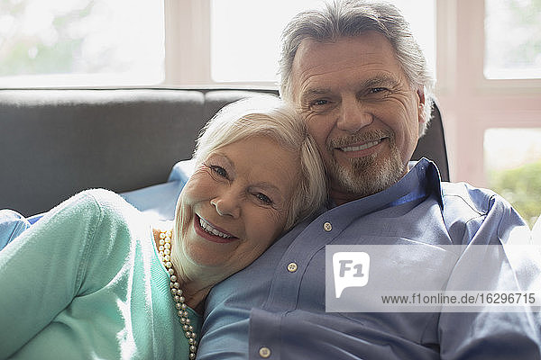 Porträt eines glücklichen Seniorenpaares beim Kuscheln auf dem Wohnzimmersofa