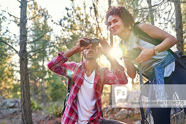 Neugieriges junges Wandererpaar mit Fernglas und Kamera in sonnigen Wäldern