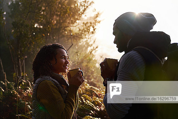 Glückliches junges Wanderpaar trinkt Kaffee in sonnigen Wäldern