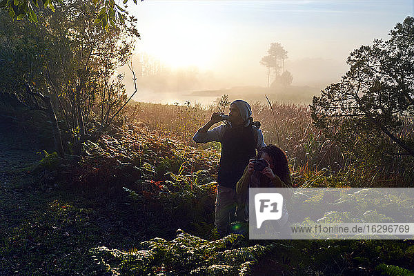 Neugieriges junges Paar wandert mit Fernglas und Kamera in sonnigen Wäldern