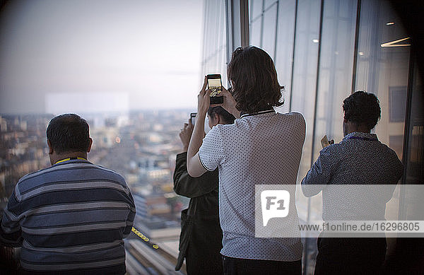 Business people using camera phones at urban office window