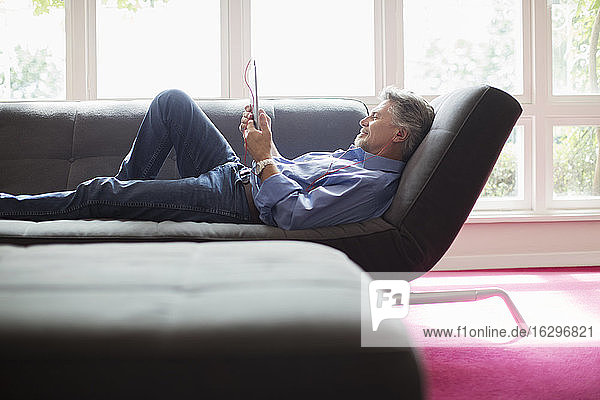 Älterer Mann entspannt sich mit digitalem Tablet auf Wohnzimmersofa
