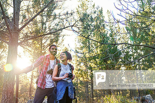 Happy young couple hiking with camera and binoculars in sunny woods