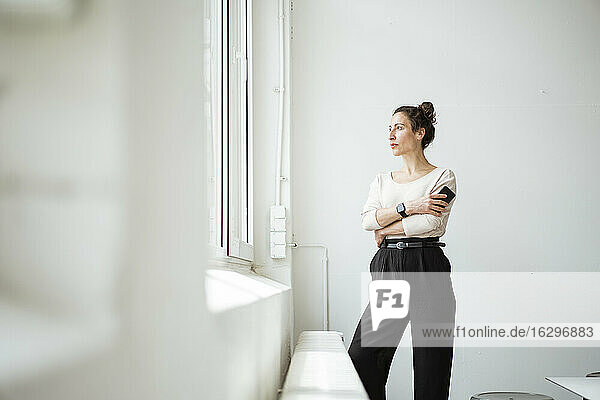 Thoughtful businesswoman with smart phone looking through window