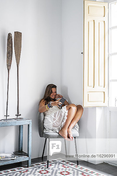 Lächelnde Frau mit Smartphone  die zu Hause auf einem Sessel sitzt