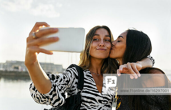 Junge Frau küsst Freund während der Einnahme selfie gegen klaren Himmel