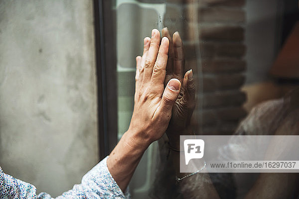 Nahaufnahme eines Paares  dessen Hände sich durch das Fenster eines Cafés berühren