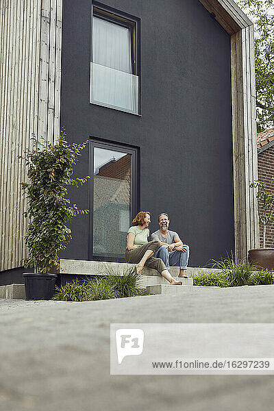 Fröhliches Paar sitzt auf den Stufen vor einem kleinen Haus