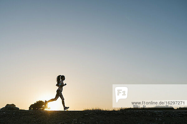 Silhouette einer Frau  die bei Sonnenuntergang gegen den klaren Himmel läuft