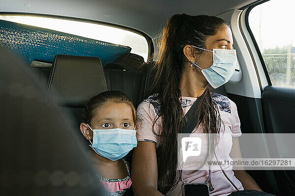 Mutter und Tochter mit Gesichtsmaske auf dem Rücksitz eines Autos
