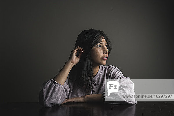 Nachdenkliche Frau mit schwarzem Haar sitzt am Tisch an der Wand