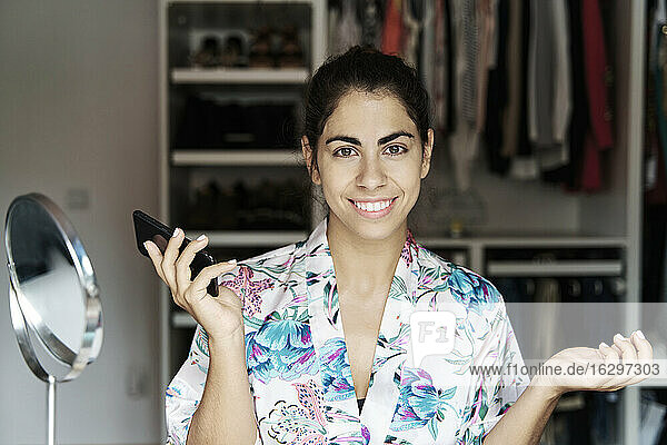 Lächelnde junge Frau  die ihr Smartphone hält  während sie zu Hause sitzt