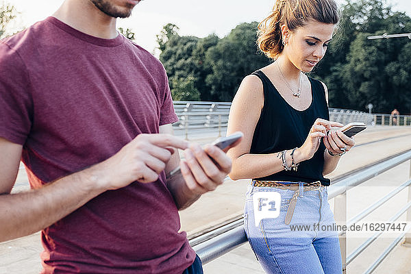 Pärchen benutzt Smartphones auf einer Brücke