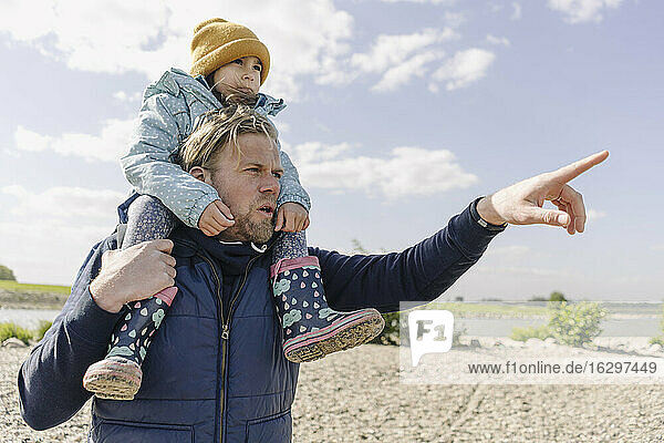 Father carrying daughter on shoulder while point at Rhine river