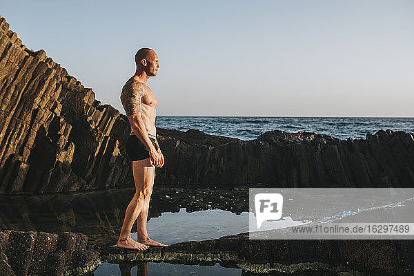 Muscular man in underpants standing on rocks by the sea