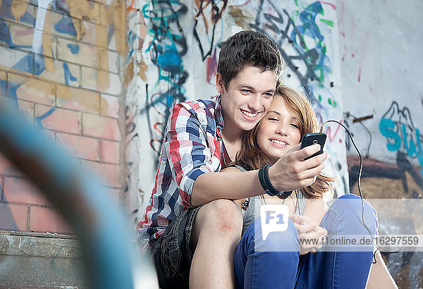 Germany  Berlin  Teenage couple using mobile phone  smiling