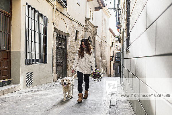 Frau hält Blumenstrauß beim Spaziergang mit Hund auf der Straße in der Stadt