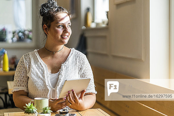 Thoughtful young woman with digital tablet sitting at table in coffee shop